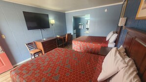 Ein Hotelzimmer mit zwei Betten, einem Schreibtisch, einem Stuhl und einem an der Wand befestigten Fernseher.