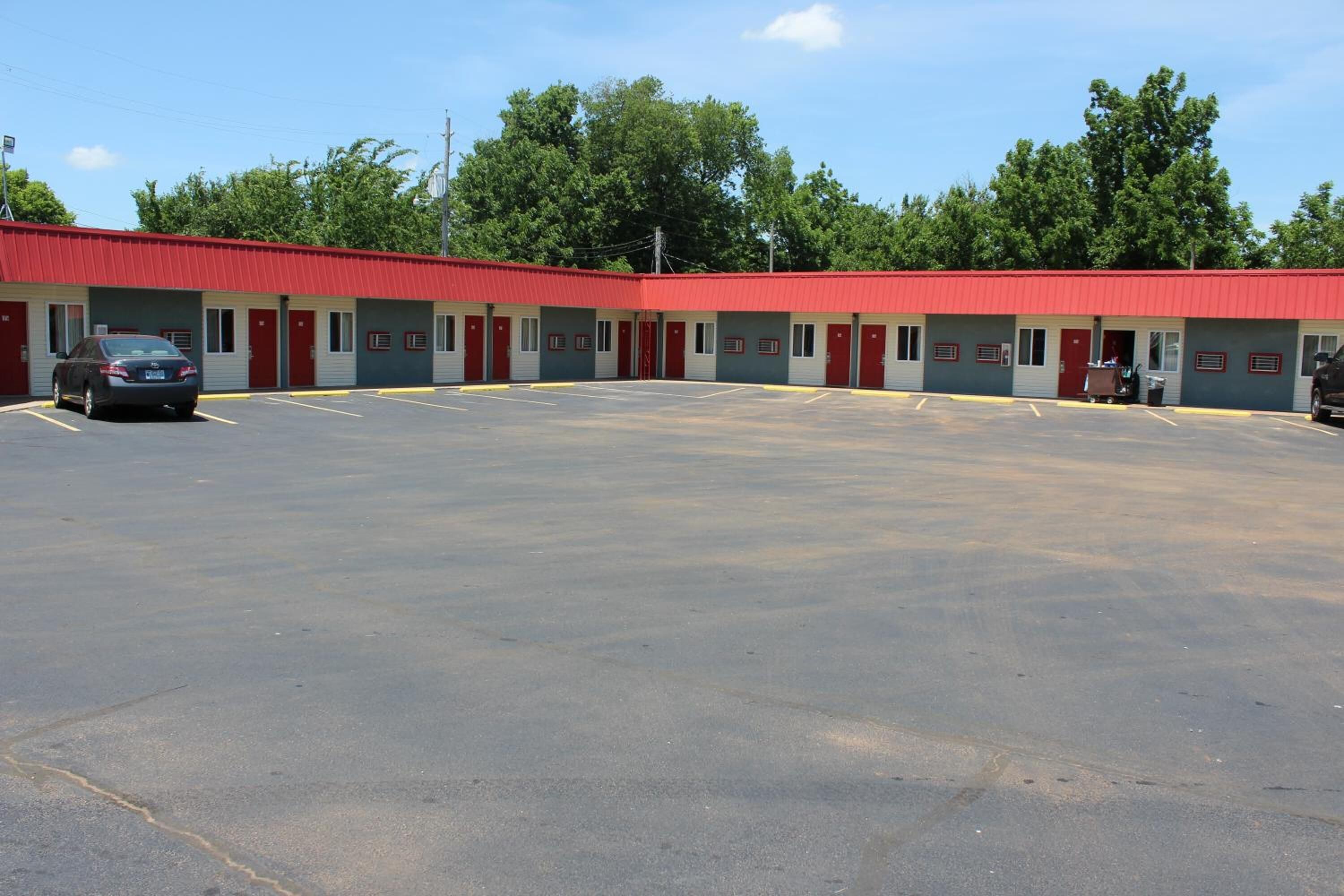 Un motel con tetto rosso e diverse camere, un parcheggio e alberi sullo sfondo.
