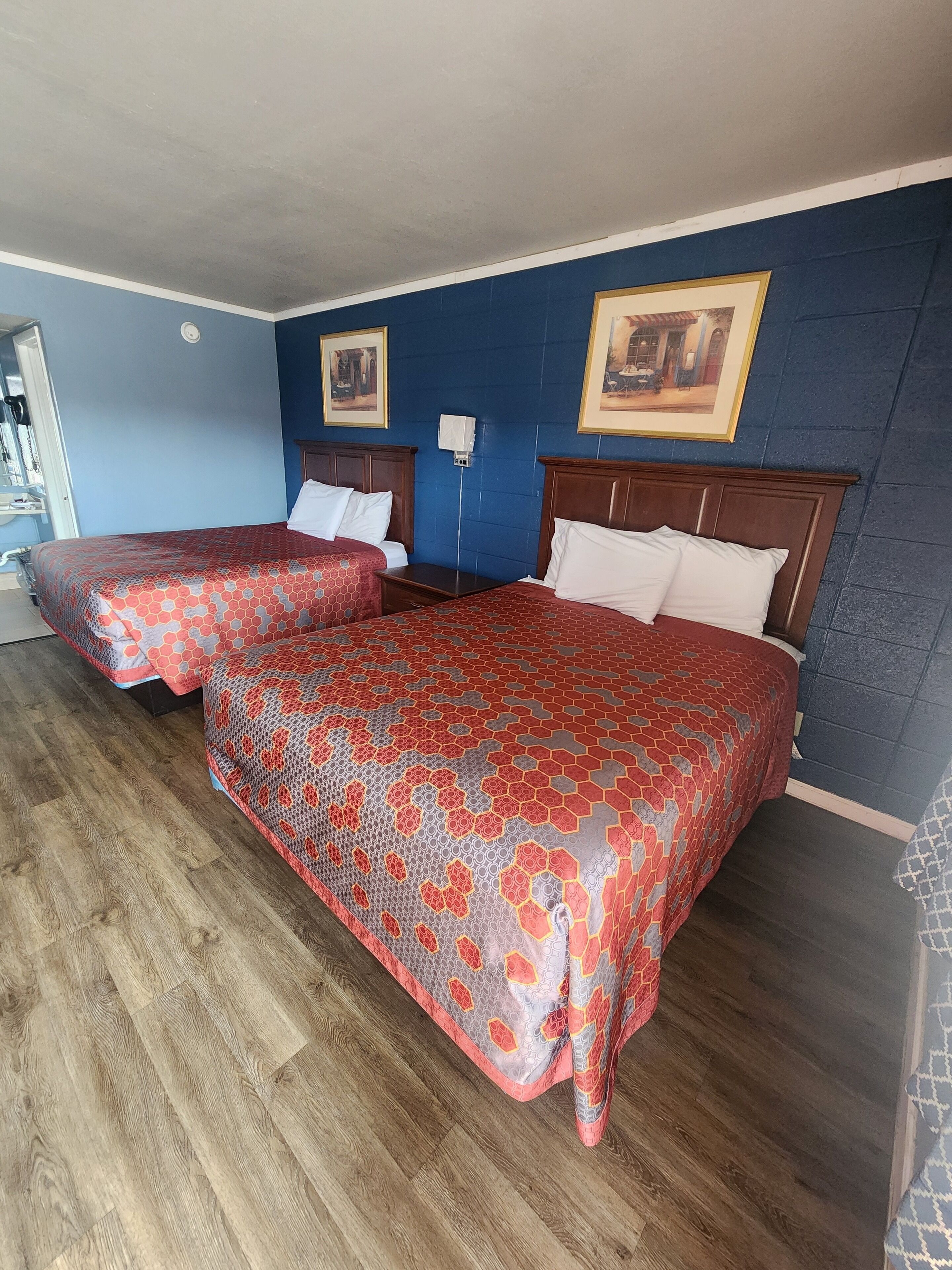 Une chambre d’hôtel avec deux lits, un plancher en bois, des murs bleus et des tableaux encadrés accrochés au mur.