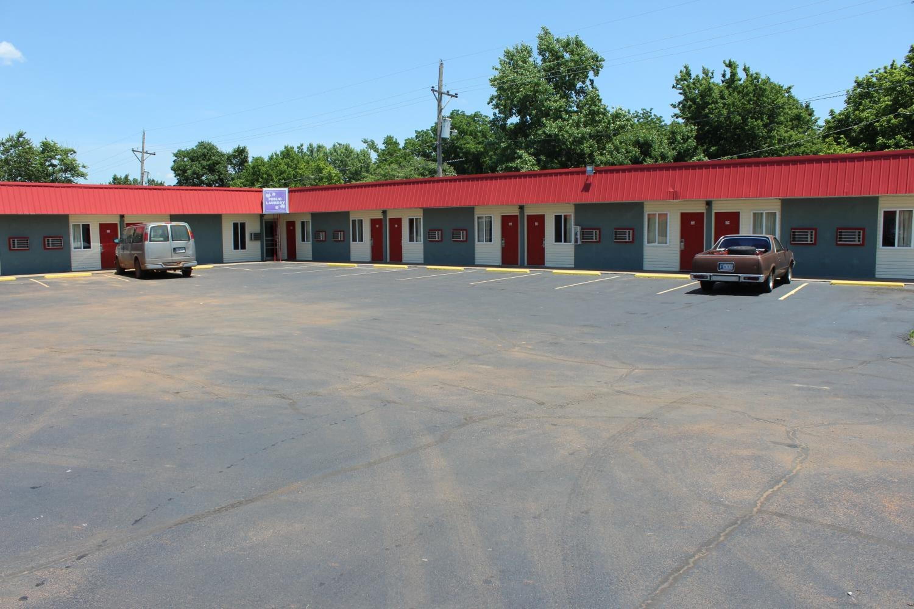 A motel with a red roof, multiple rooms, and a parking lot.