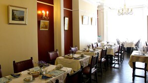 A dining area with tables set for service, framed artwork on the walls, and a chandelier. - Melrose Guest House (Douglas)