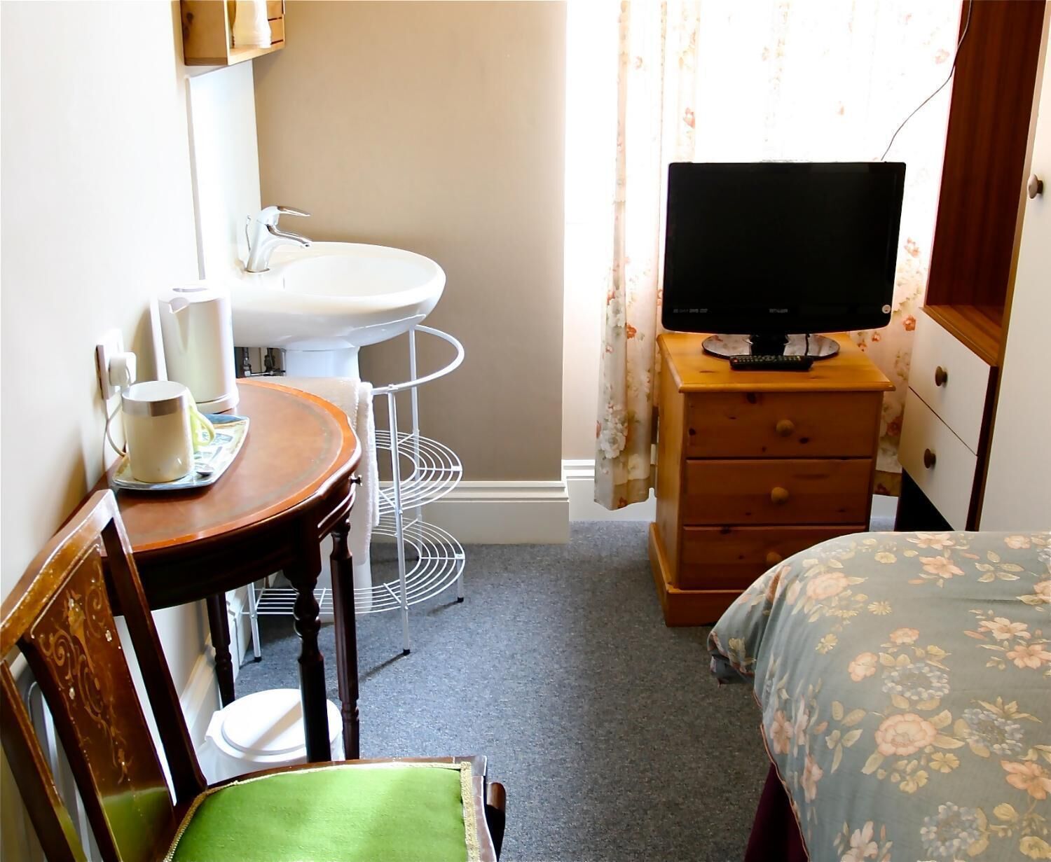 Une petite pièce, de taille modeste, comprenant un lit, un téléviseur posé sur une commode, un lavabo et une chaise.