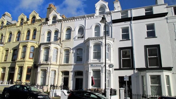 A row of Victorian-style townhouses with arched windows and a white facade. - Melrose Guest House (Douglas)