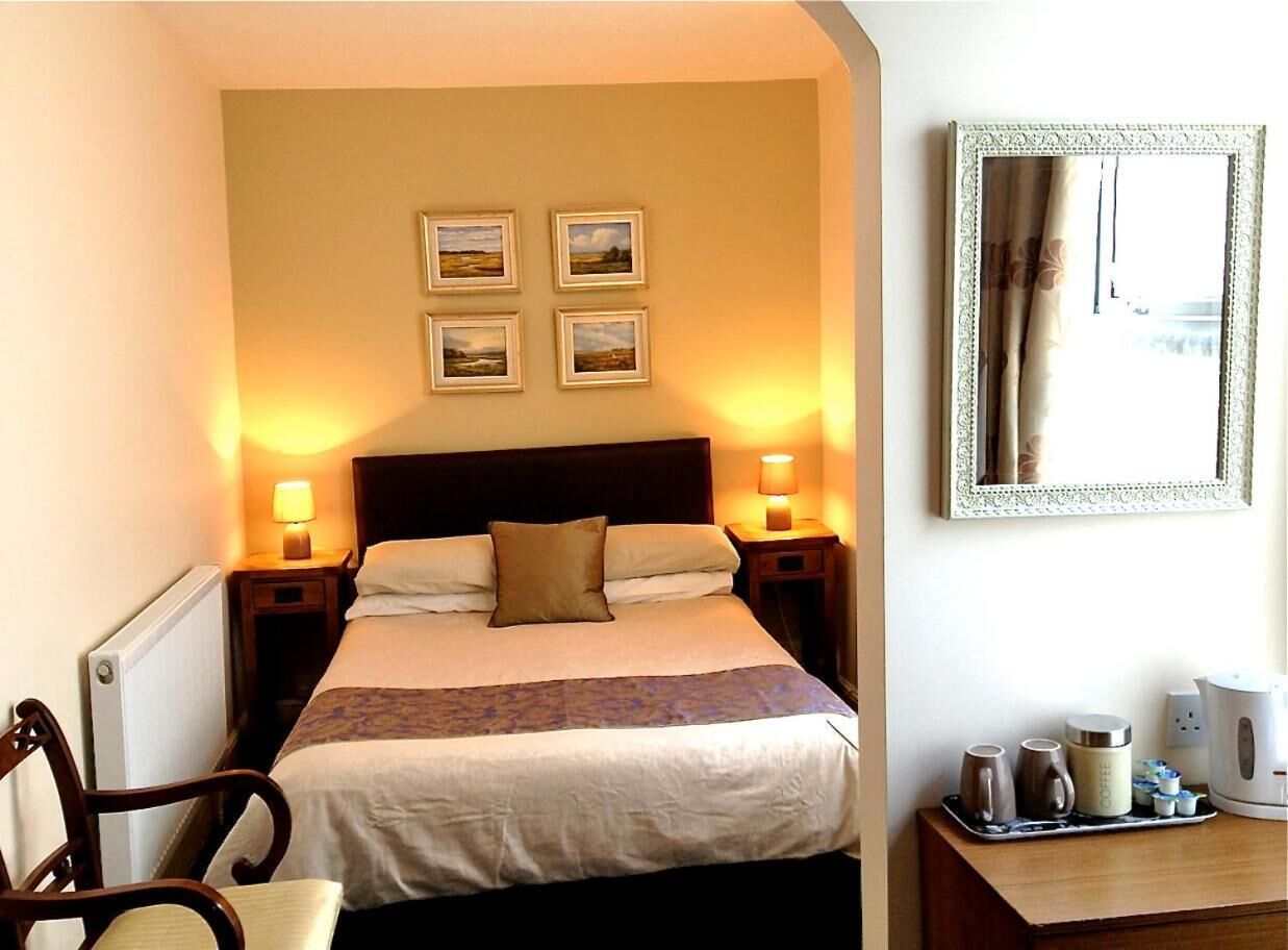 A neatly arranged hotel room with a bed, bedside lamps, a coffee station, and framed pictures on the wall.