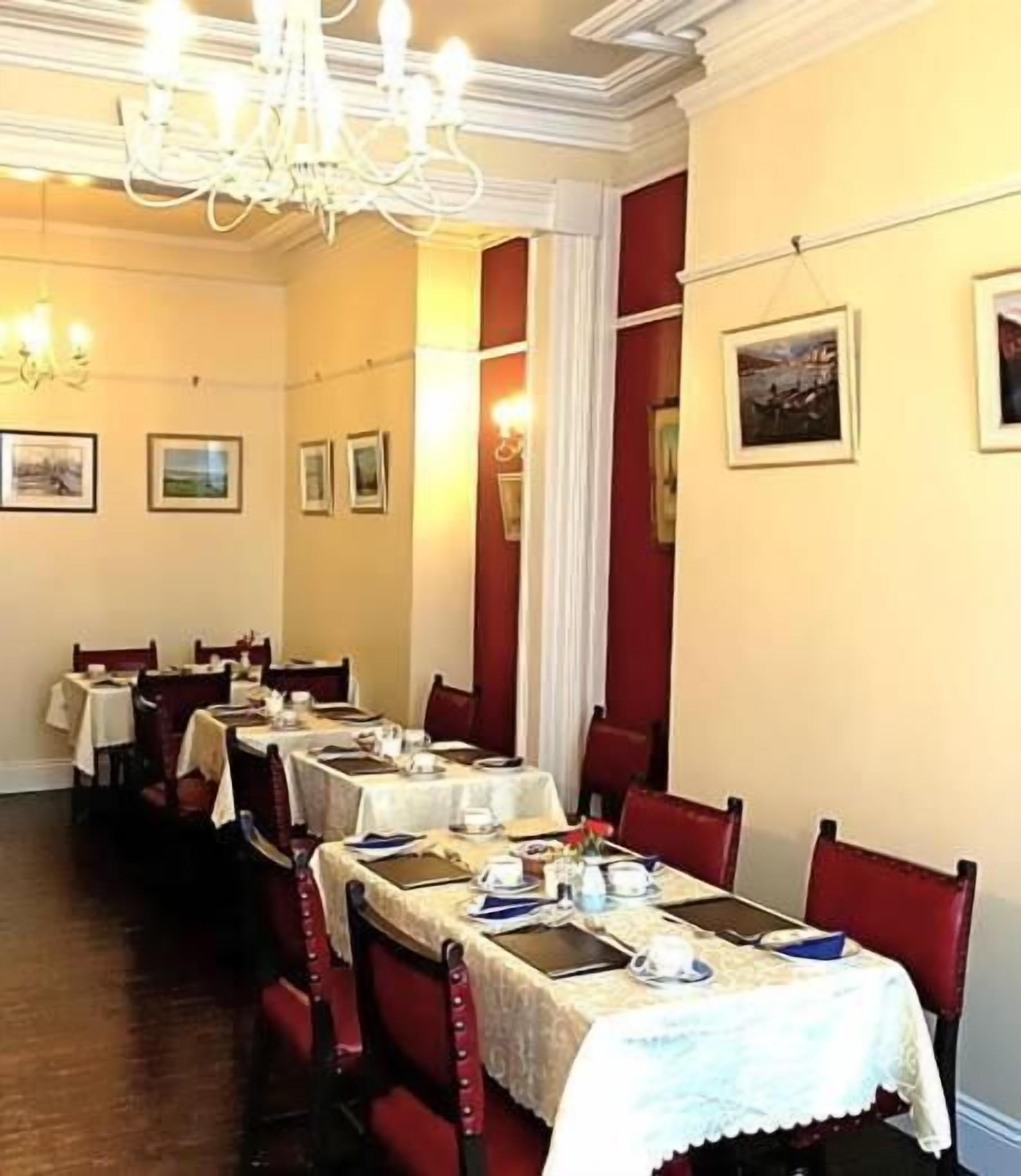 A dining area with multiple tables set for service, red upholstered chairs, and a chandelier.