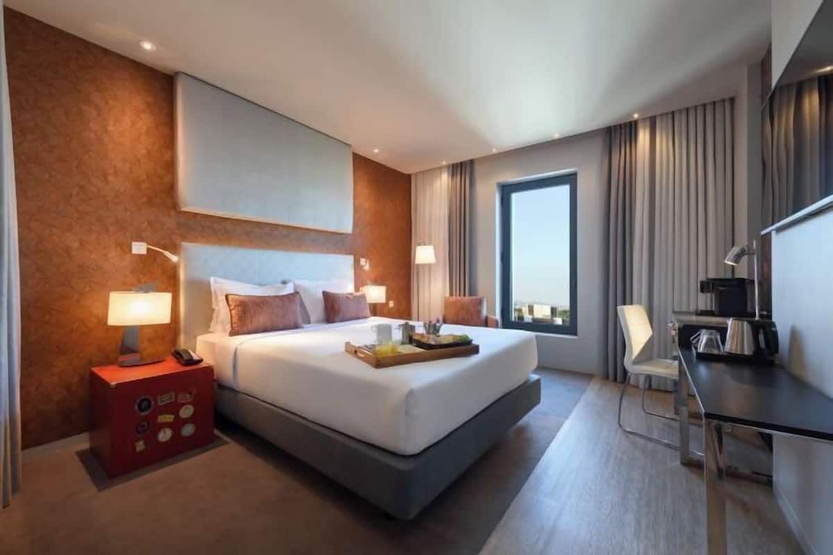 Ein modernes Hotelzimmer mit einem großen Bett, Nachttischlampen, einem Schreibtisch und Blick auf die Stadt.