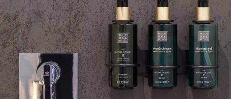 Un dispensador montado en la pared con tres botellas de productos para el cabello con la etiqueta "The Ritual of Dao", incluyendo acondicionador, champú y gel de ducha.