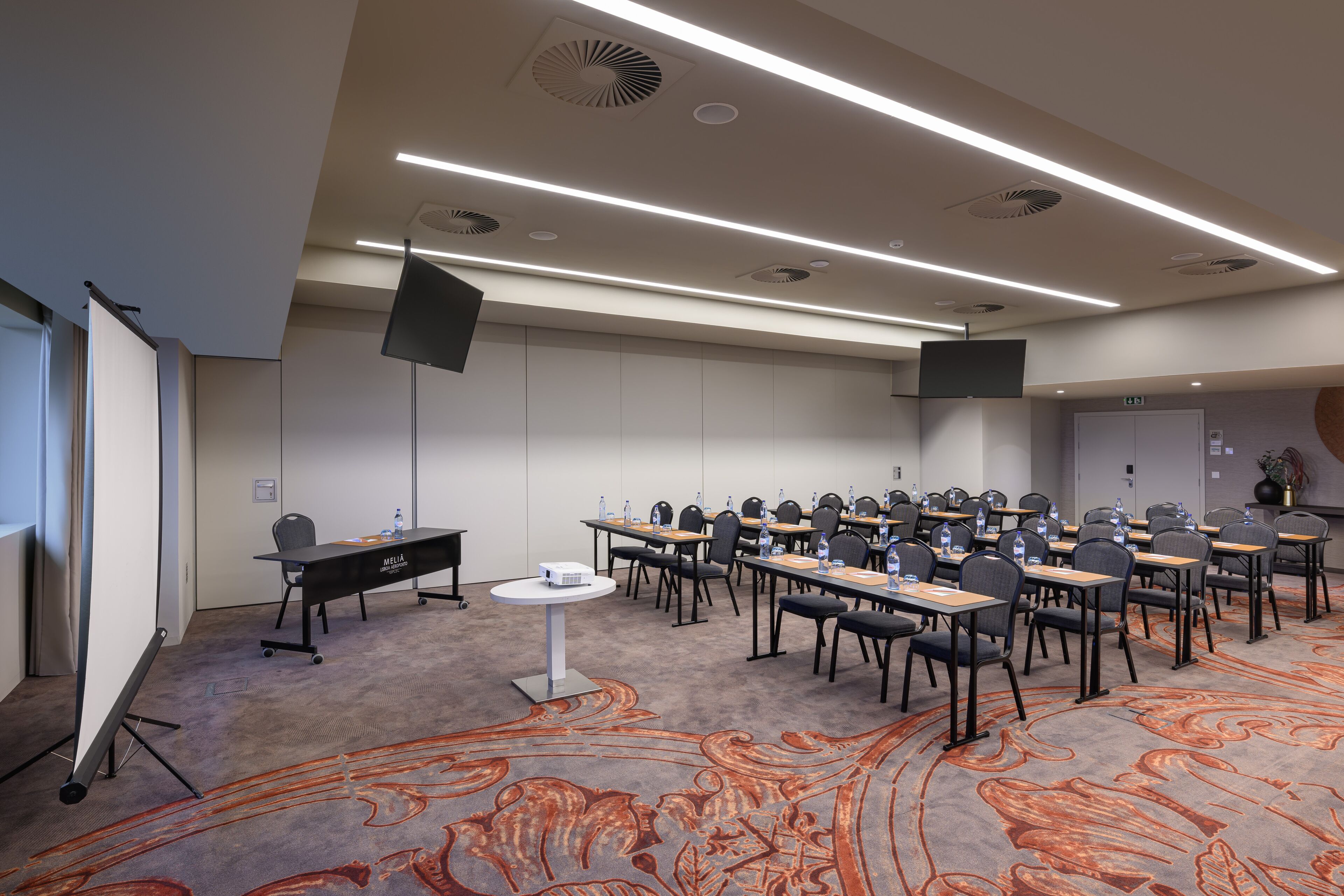 A conference room with a carpeted floor, multiple tables, chairs, a projector, and a whiteboard.