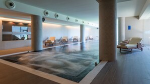 Un área de piscina interior moderna con sillones de descanso y una recepción.