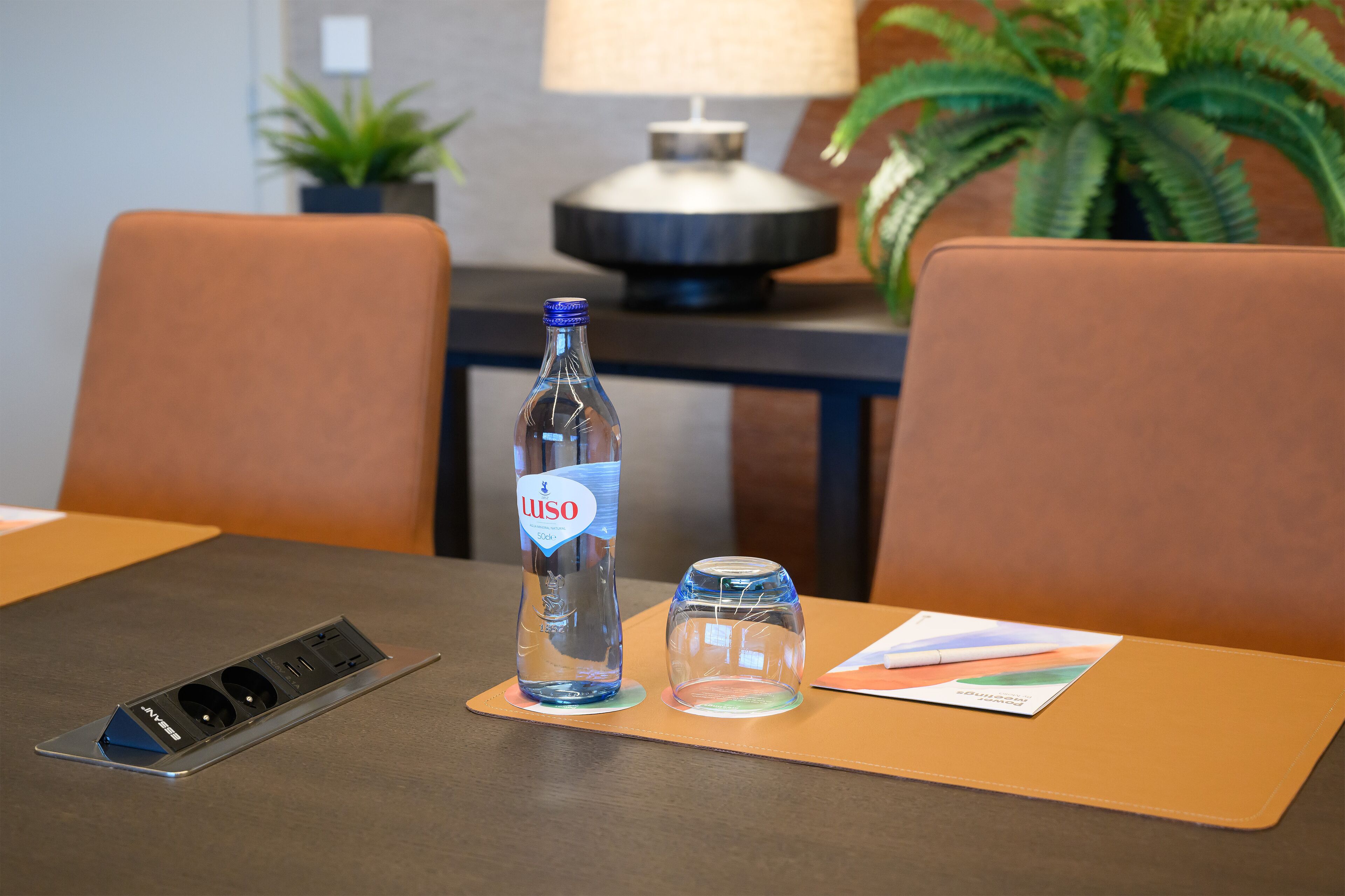 A hotel room with a table set for two, a bottle of water, a glass, and a power strip.