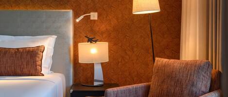 A hotel room with a bed, a nightstand with a lamp, a chair, and a wooden textured wall.