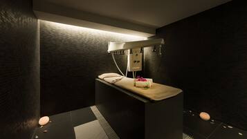 Un'area spa moderna con un lettino da massaggio, un asciugamano e un piccolo bouquet di fiori.
