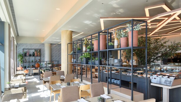 Un restaurante moderno con diversas opciones de asientos, como mesas y sillas, y una vitrina central con productos alimenticios.
