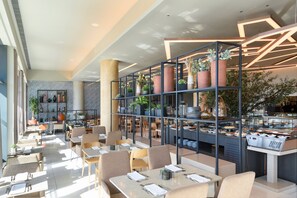 Un restaurant moderne offrant différents types de sièges, notamment des tables et des chaises, ainsi qu’un présentoir central où sont exposés les plats proposés.