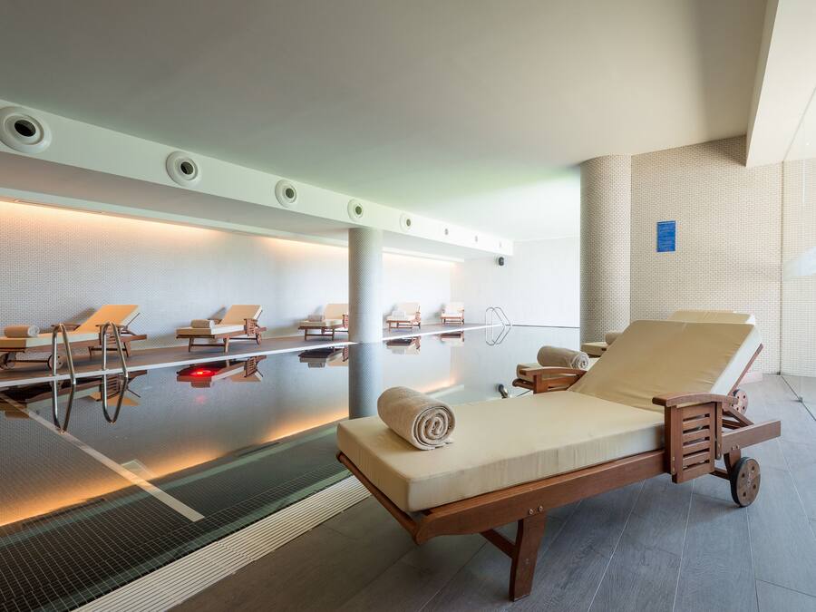 A modern spa with a glass-enclosed pool, multiple sun loungers, and a massage table.