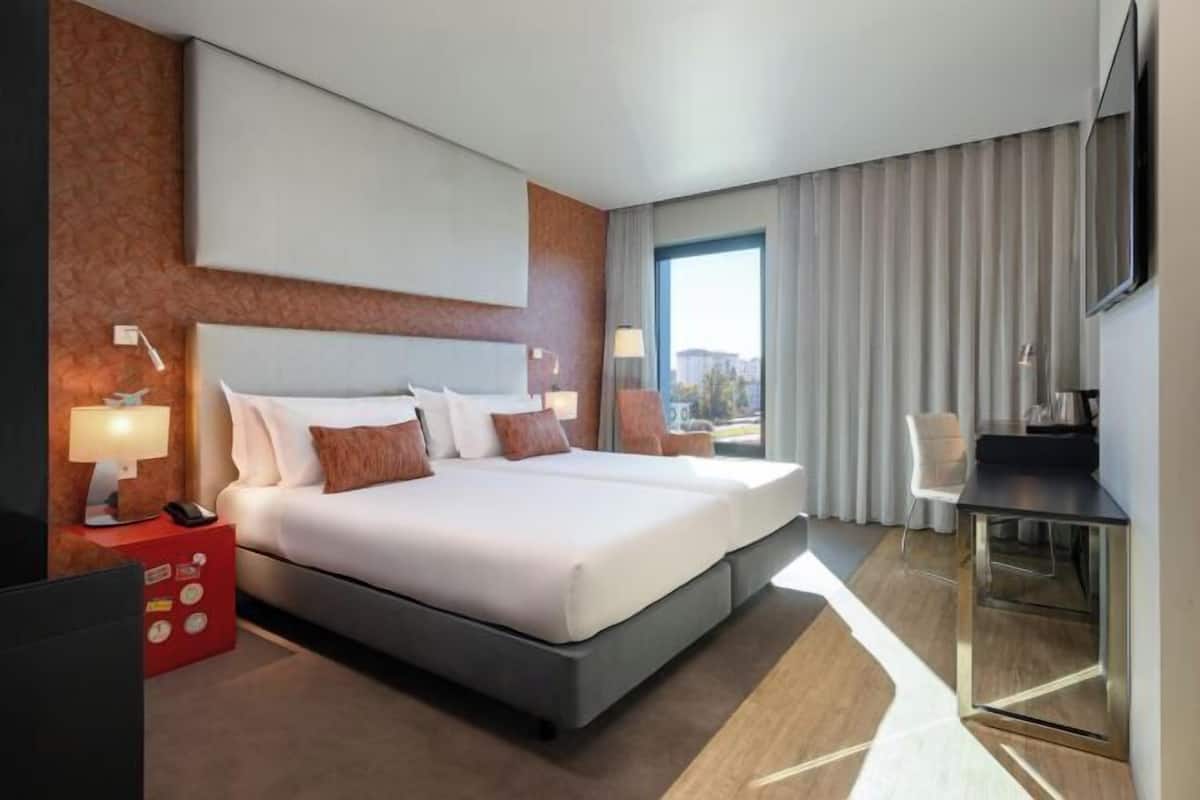 Ein modernes Hotelzimmer mit einem großen Bett, einem Schreibtisch und Blick auf die Stadt.