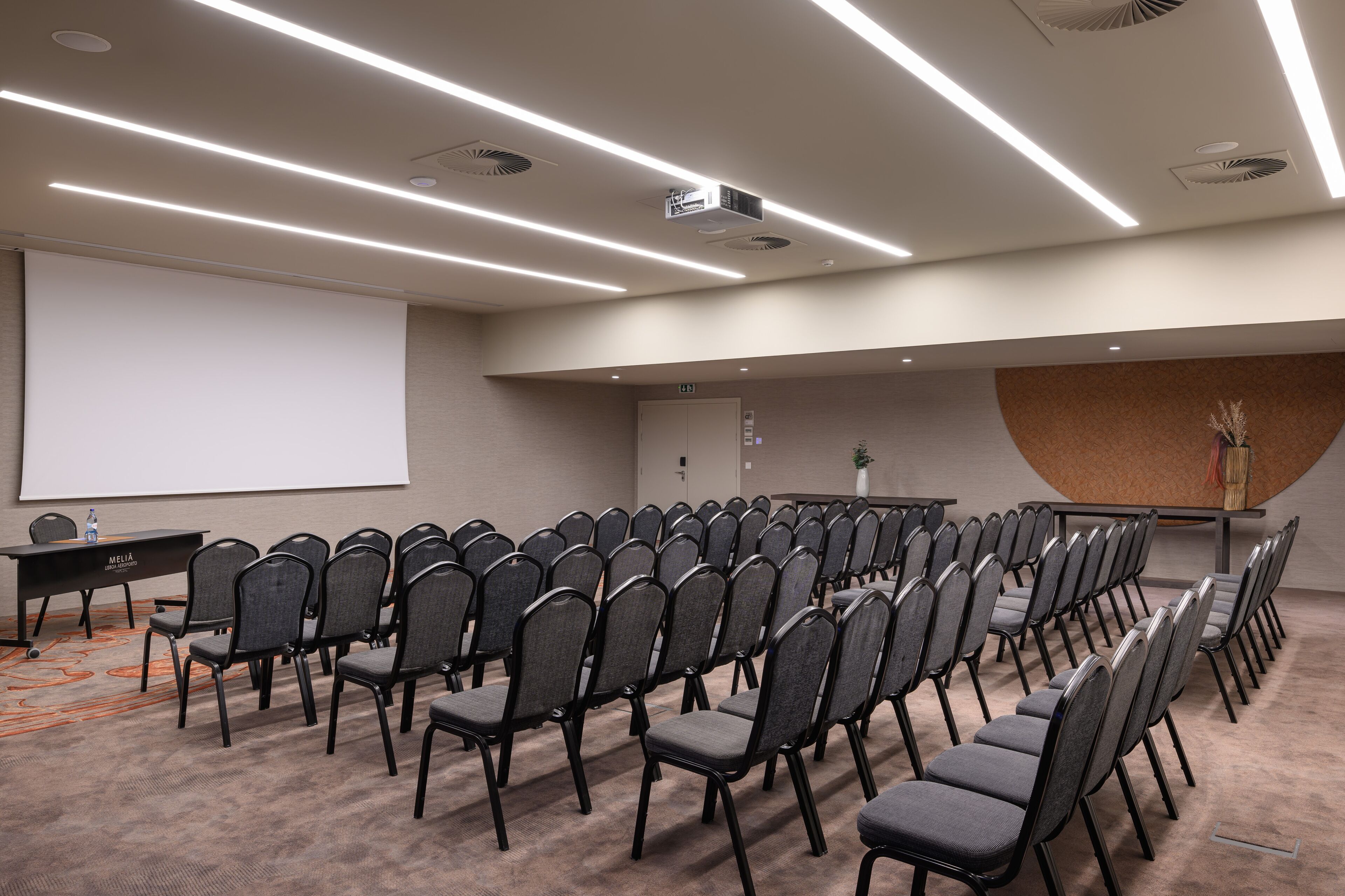 Un salón de conferencias con filas de sillas, una pantalla para proyector y un atril.