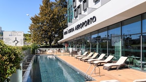 Un edificio moderno con zona de piscina, sillas de descanso y un letrero que indica servicios como 'chegadas arrivals' y 'parque parking'.