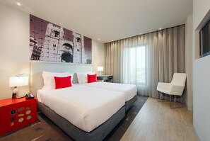 Een hotelkamer met een groot bed, twee nachtkastjes, een bureau, een stoel en een groot raam met gordijnen.