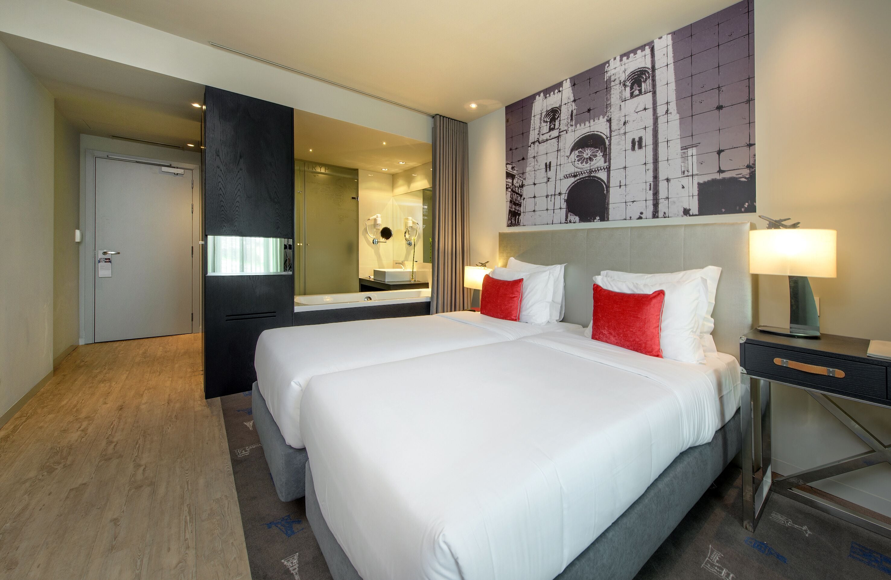 A hotel room with a large bed, a bedside table with a lamp, a mirror, and a painting on the wall.