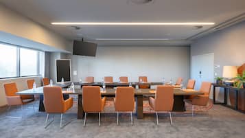 Een vergaderzaal met een lange tafel, oranje stoelen en een flatscreen televisie.