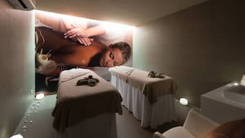 Ein Spa-Behandlungsraum mit zwei Massageliegen, einem weißen Stuhl und einem Plakat einer Massage.