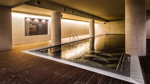 Una piscina interior moderna con suelo de madera, paredes de azulejos y una barandilla de cristal.