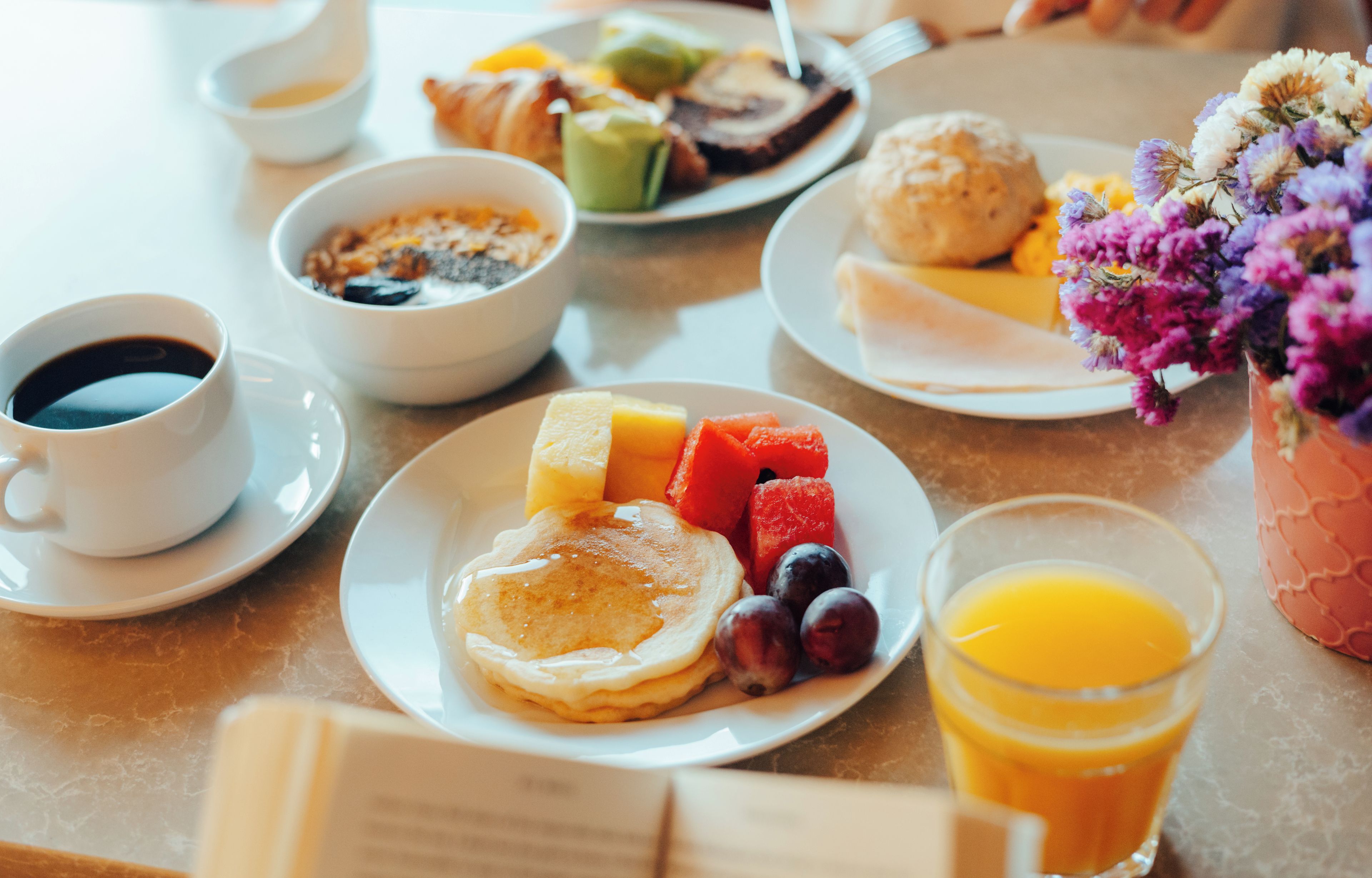 A breakfast setting with pancakes, fruits, and a glass of orange juice on a table.