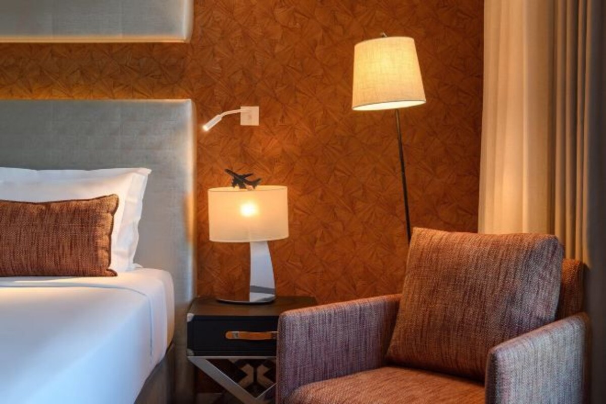 Hotelkamer met een bed, nachtkastje met lamp, stoel en wand met behang.