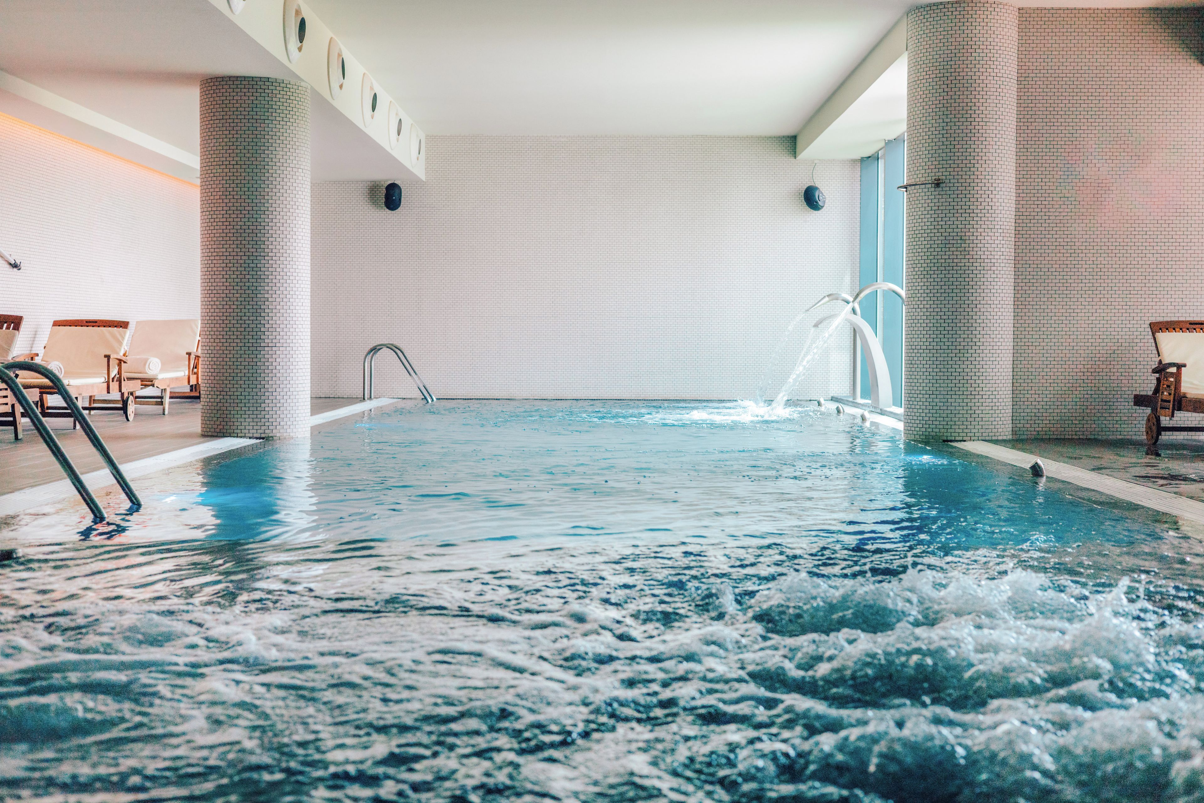 An indoor swimming pool with clear water, a diving board, and lounge chairs.