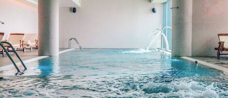 An indoor swimming pool with clear water, a diving board, and lounge chairs.
