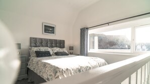 Un dormitorio con cama, mesita de noche, lámpara, un cuadro en la pared y ventana con cortinas.