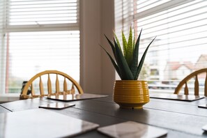 Una mesa de comedor con una maceta amarilla que contiene una planta, sillas de madera y una ventana con persianas.