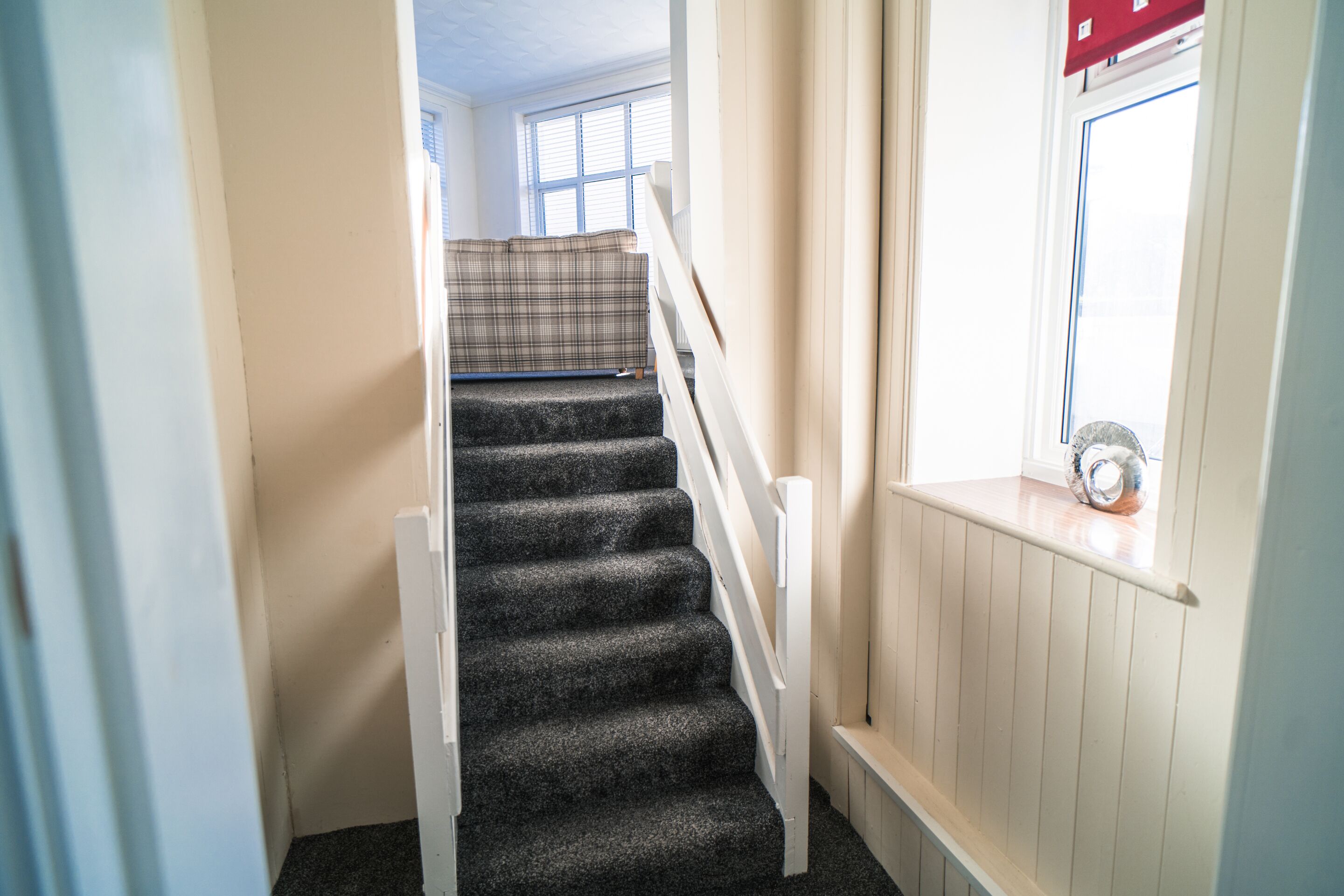 A staircase with carpeted steps, white handrails, and a window with blinds.