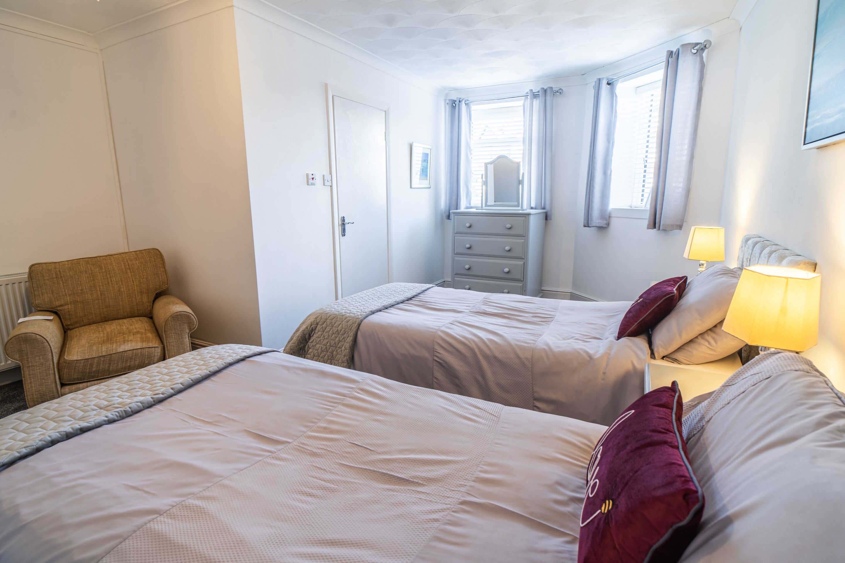 A hotel room with two beds, a chair, a dresser, and a window with curtains.