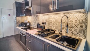 Una cocina moderna con armarios oscuros, un lavamanos de acero inoxidable y azulejos decorativos en la pared.