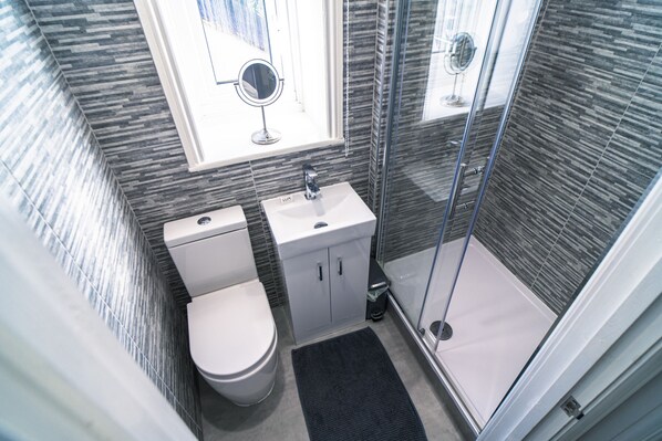 A bathroom with a toilet, sink, and shower area. - Beachmount Holiday Apartments (Colwyn Bay)