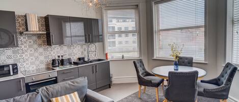 A modern kitchen with patterned backsplash, a dining area with a round table and chairs, and a gray sofa with a 'HOME' pillow.