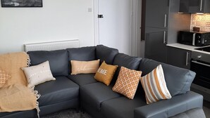 Una sala de estar moderna con un sofá modular, una chimenea y una zona de cocina.