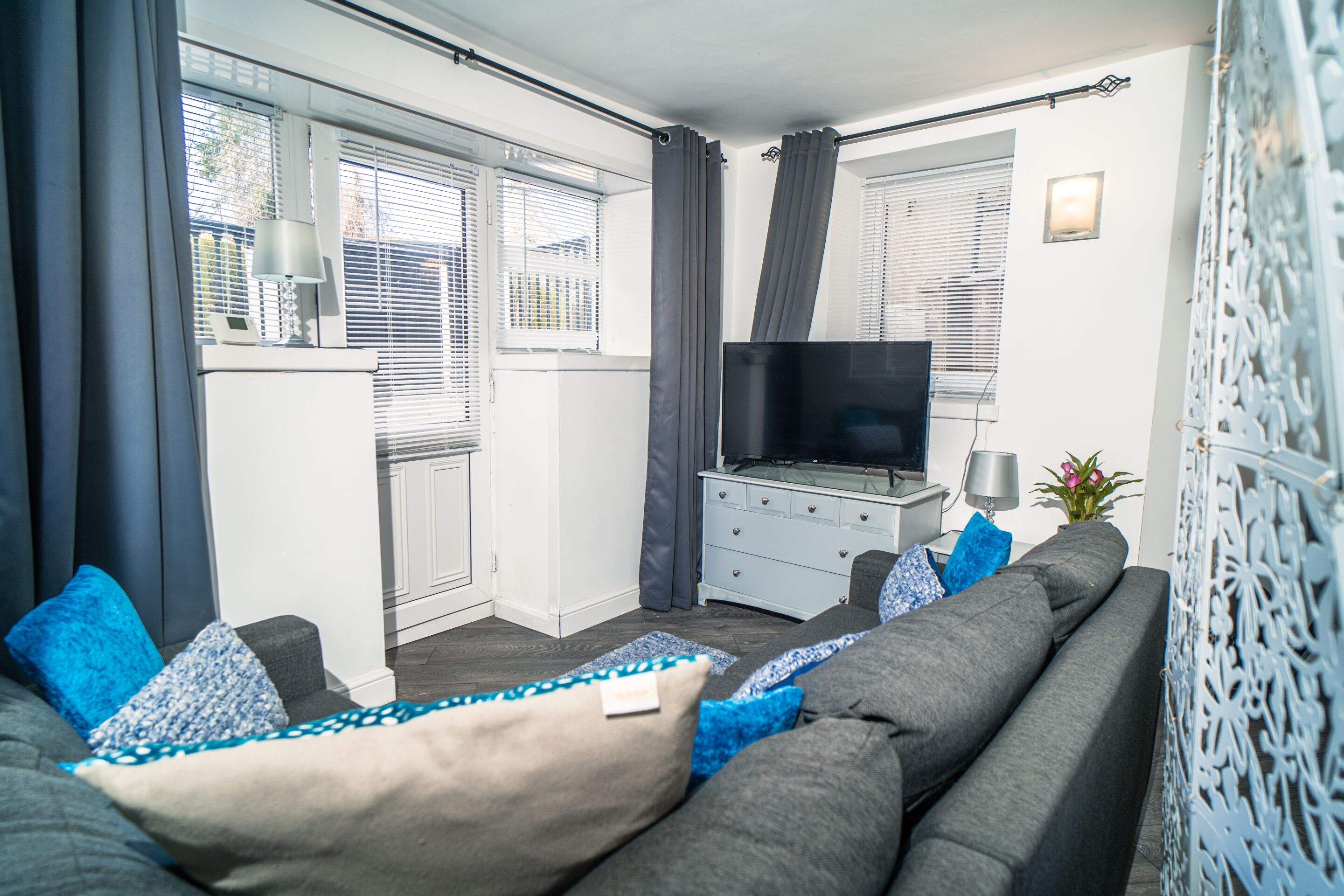 A modern living room with a grey sofa, a flat-screen TV, and a small white cabinet.