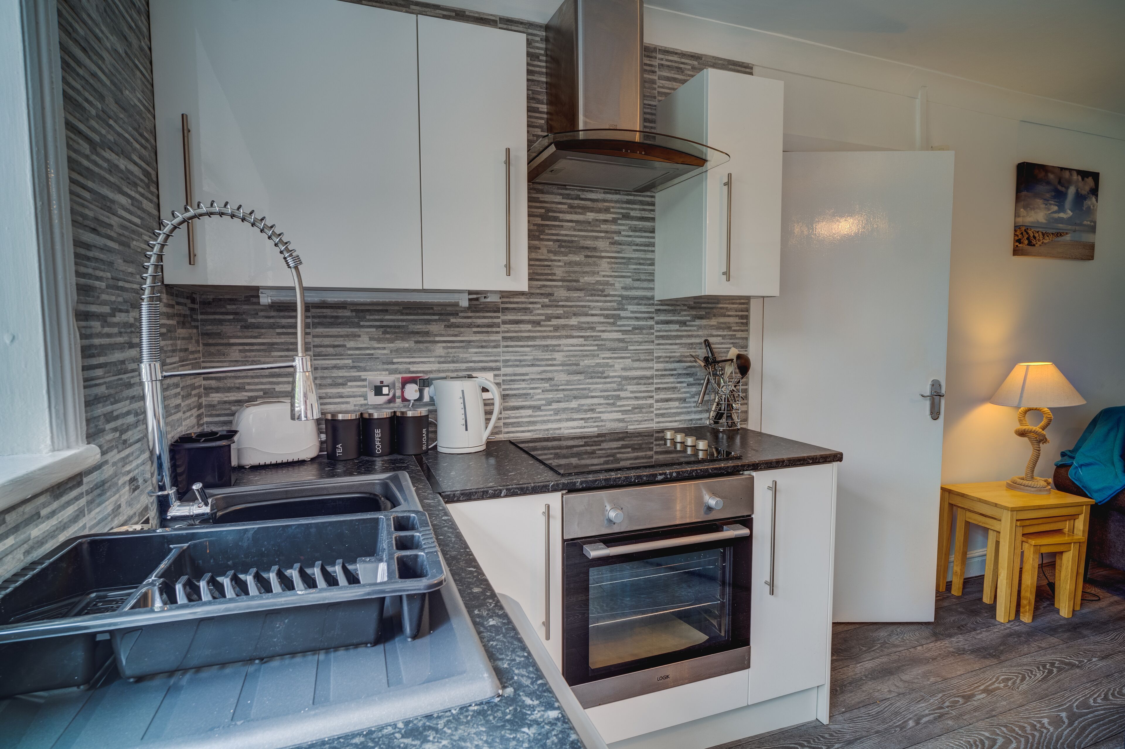 Una cocina compacta con gabinetes blancos, horno empotrado, extractor de acero inoxidable y un grifo moderno.