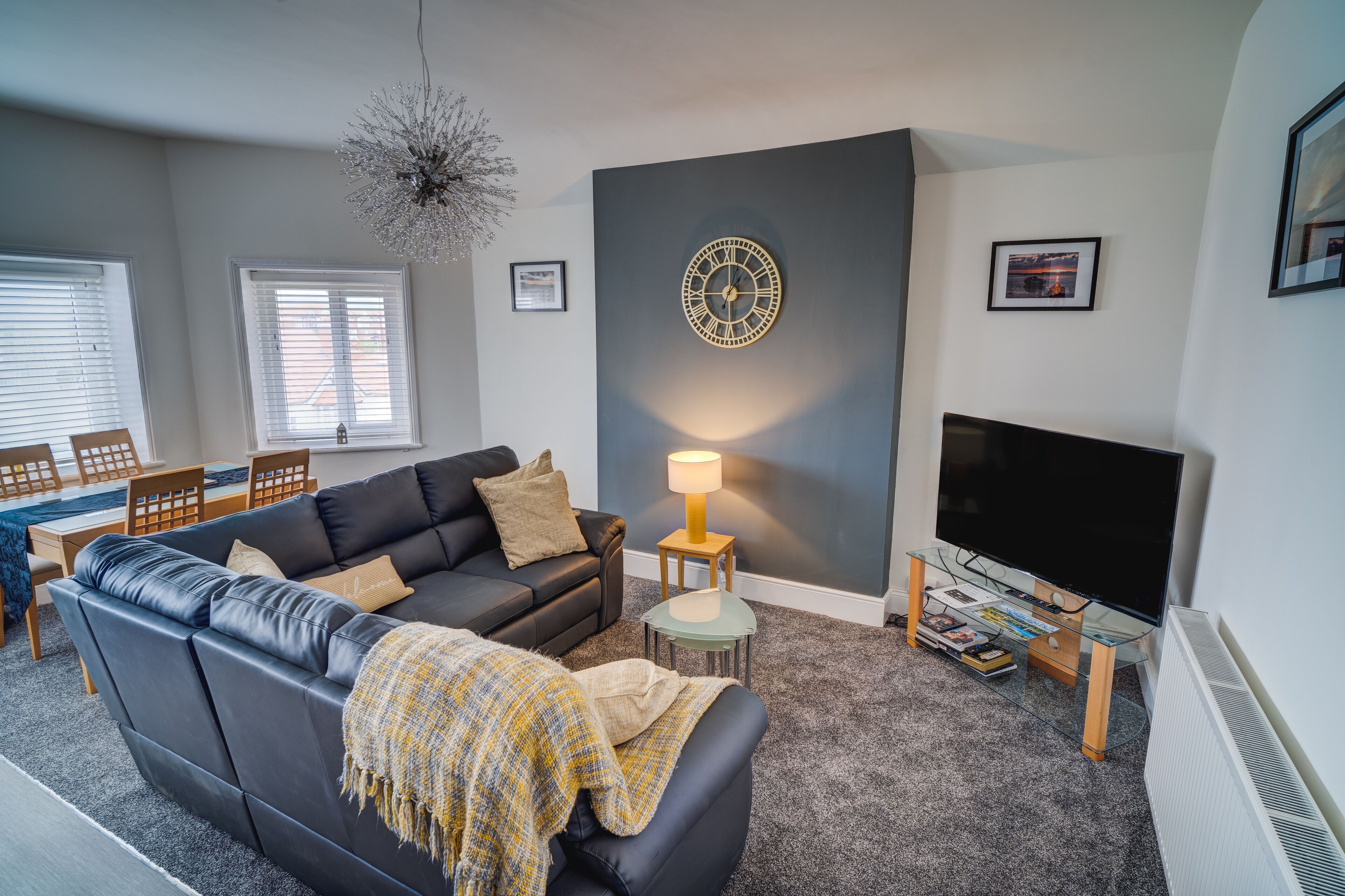 A living room with a black leather sofa, a glass coffee table, a TV, and a wall clock.