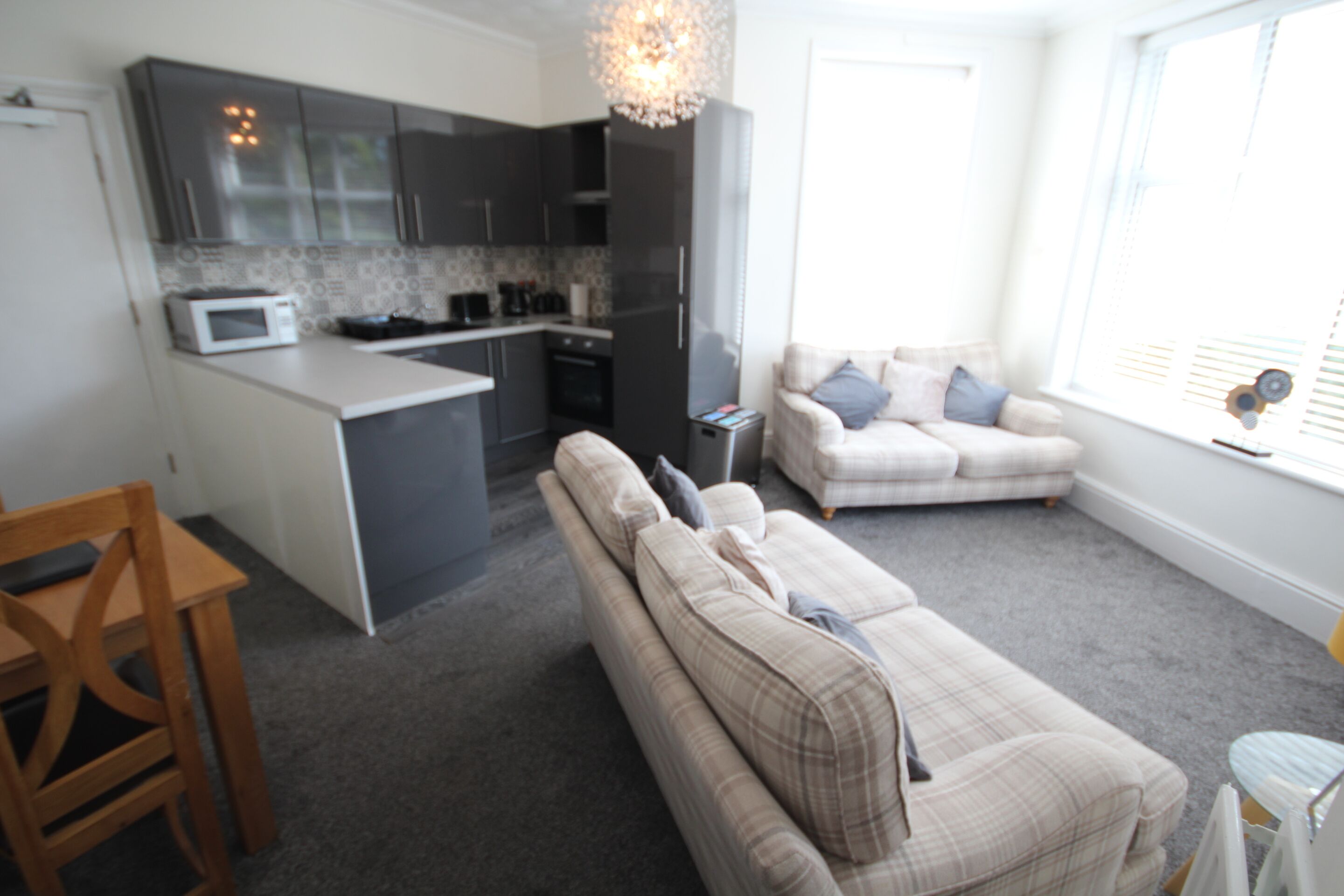 A modern kitchen with dark cabinets, a microwave, and a central island. There is a beige sofa with plaid cushions in a living area with a window.