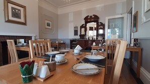 Un comedor con una mesa de madera para cuatro personas, sillas, una chimenea y cuadros en las paredes.