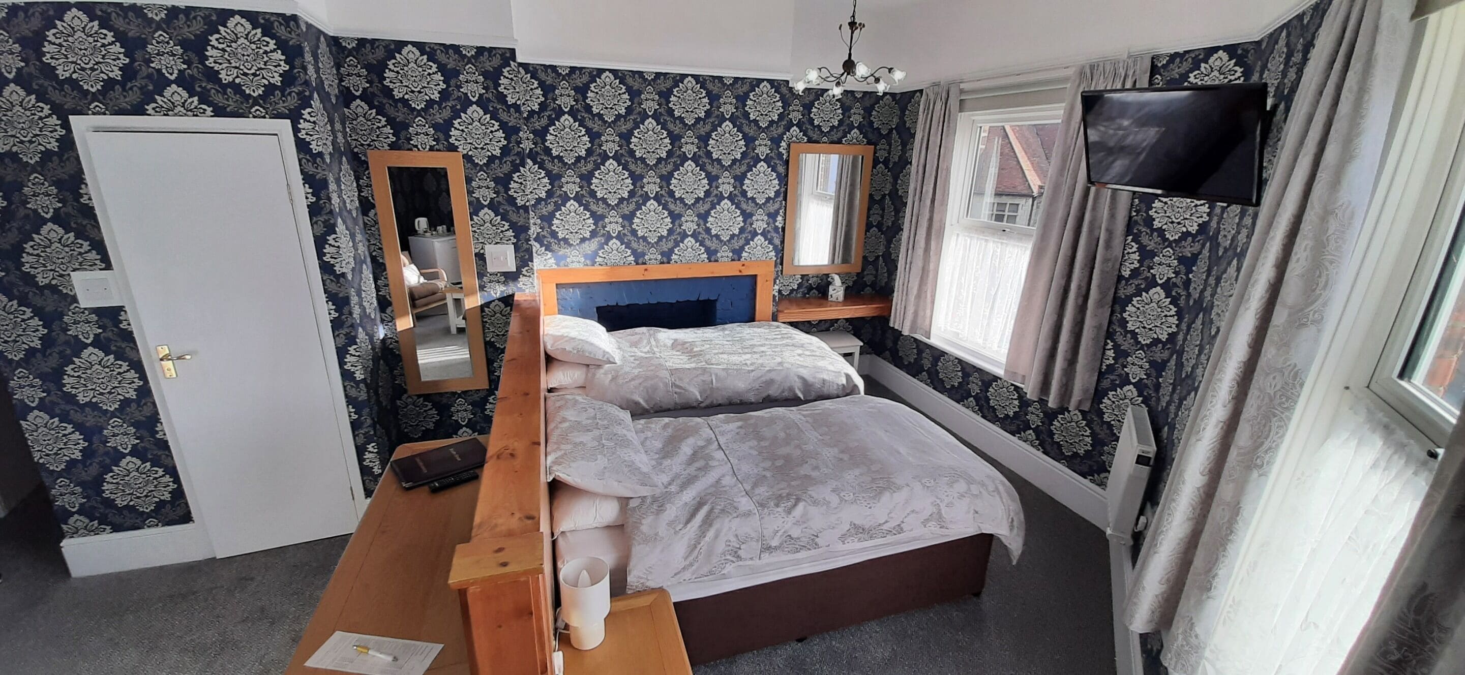 Ein Schlafzimmer mit Bett, Nachttischen, einem Spiegel, einem Fernseher und einem Fenster mit Vorhängen.