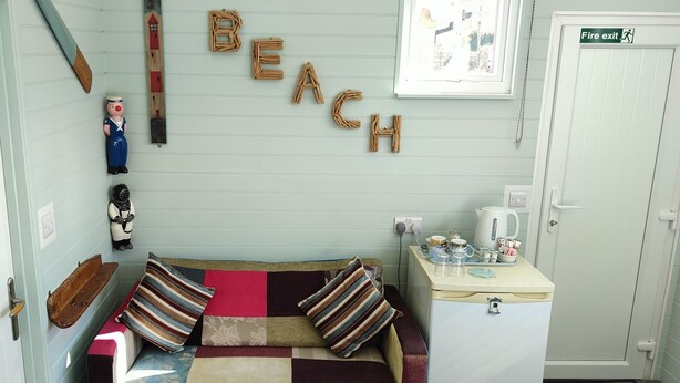 Una habitación acogedora con un sofá, almohadas, una mesita con una tetera y una pared que dice 'BEACH'.