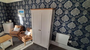 Una habitación con papel tapiz estampado, un armario blanco, un banco de madera, una silla y un radiador.