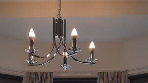 Una habitación con dos sillones, una mesita, un candelabro y un amplio ventanal con cortinas.