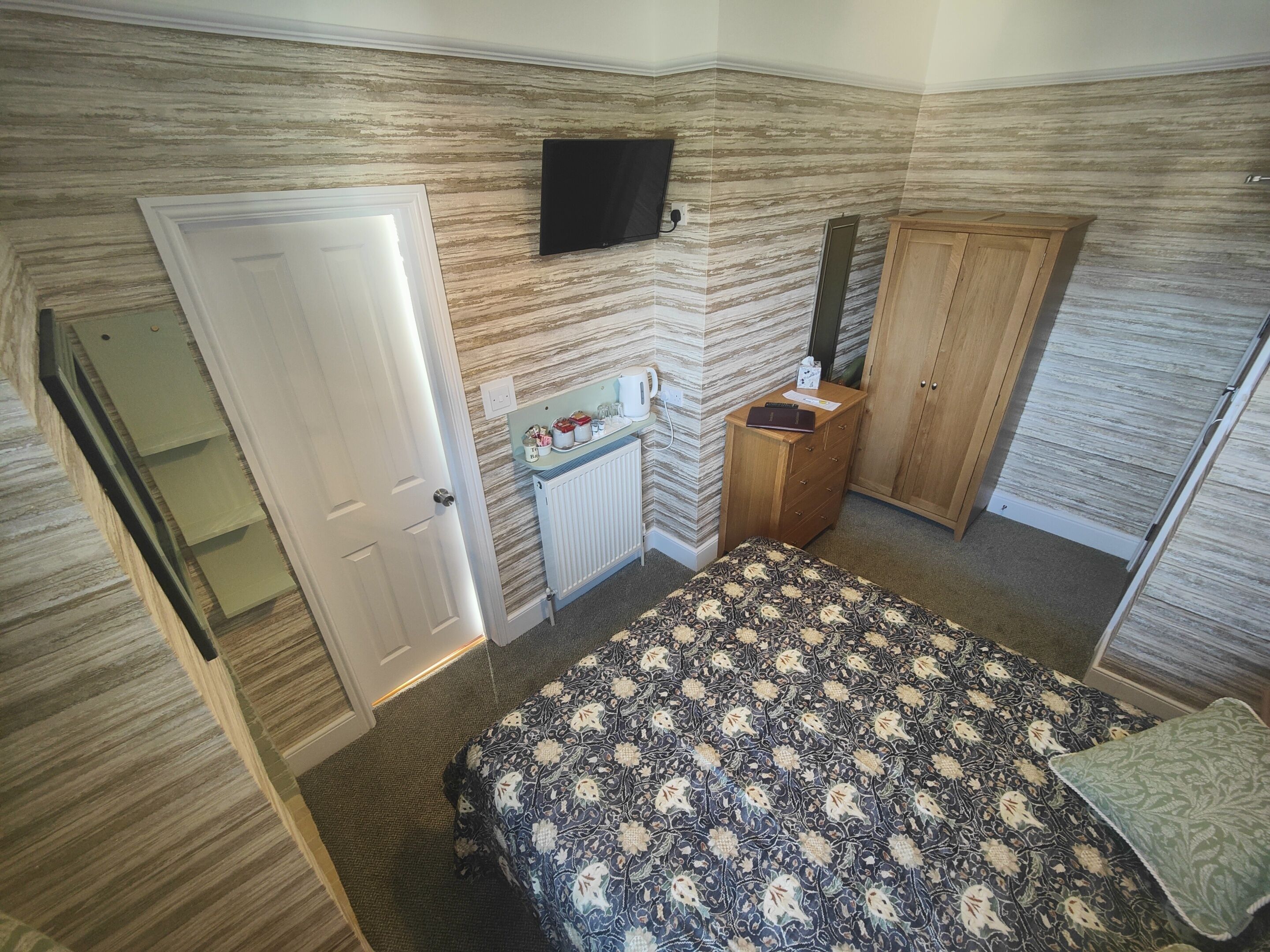 Un dormitorio con cama, armario, espejo, televisor y radiador.