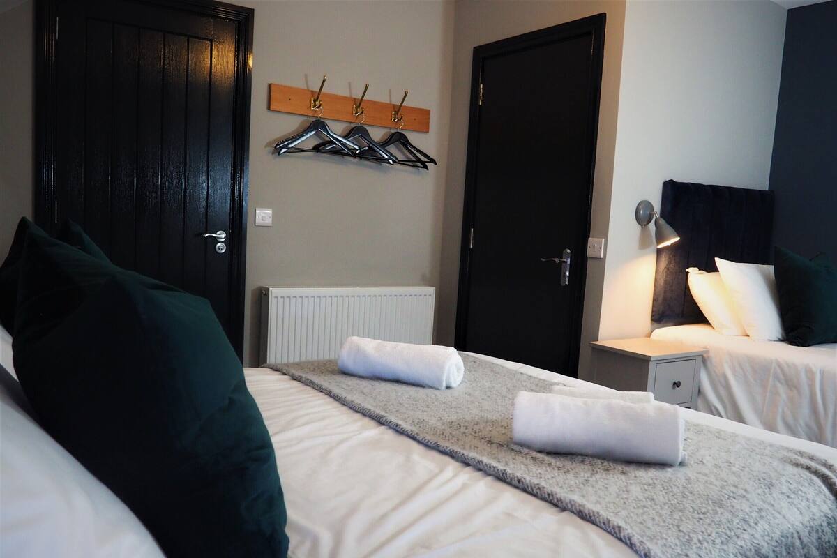 A hotel room with two beds, a coat rack, a door, and a bedside lamp.